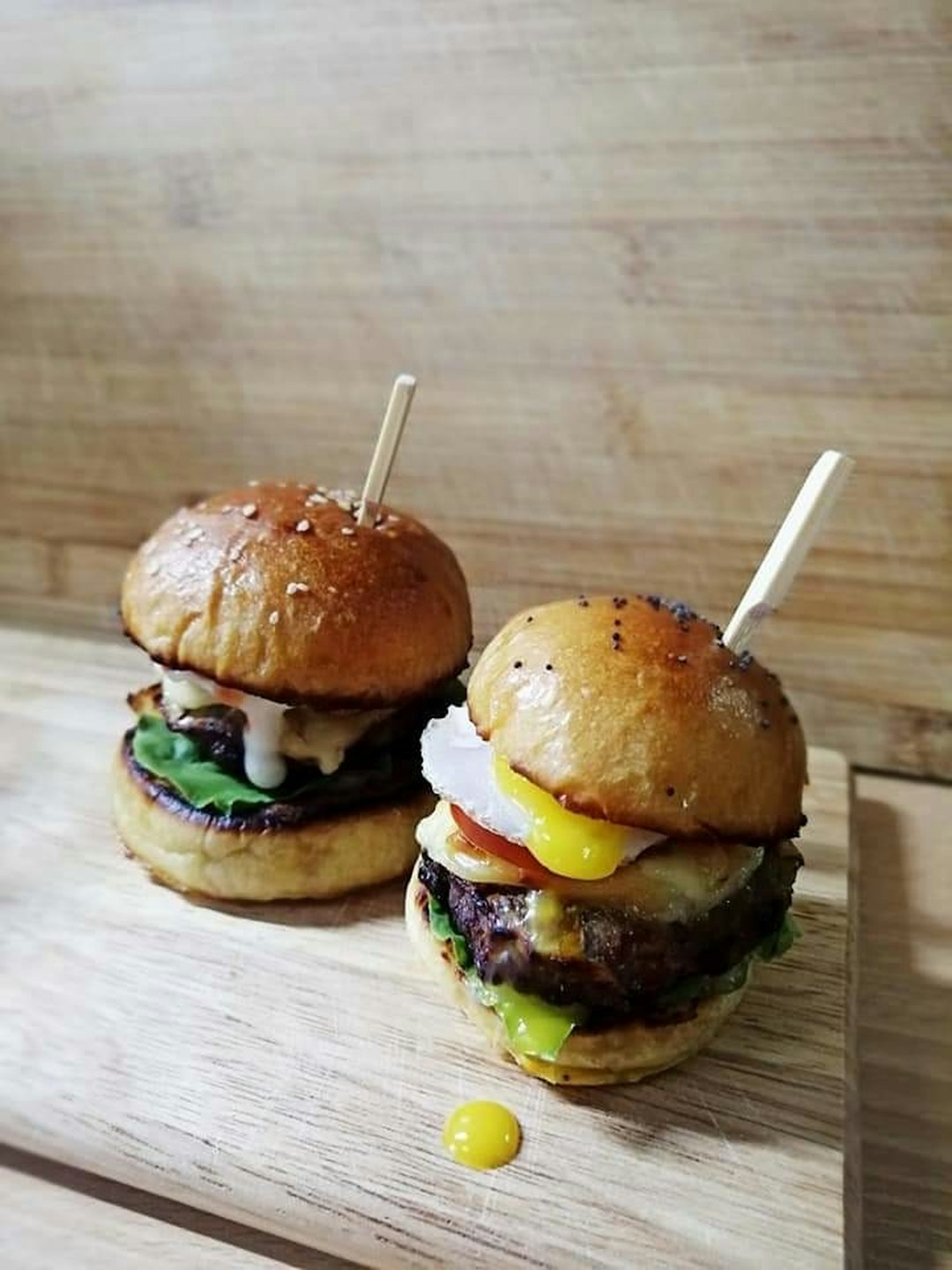 Two mini gourmet burgers on a wooden cutting board.