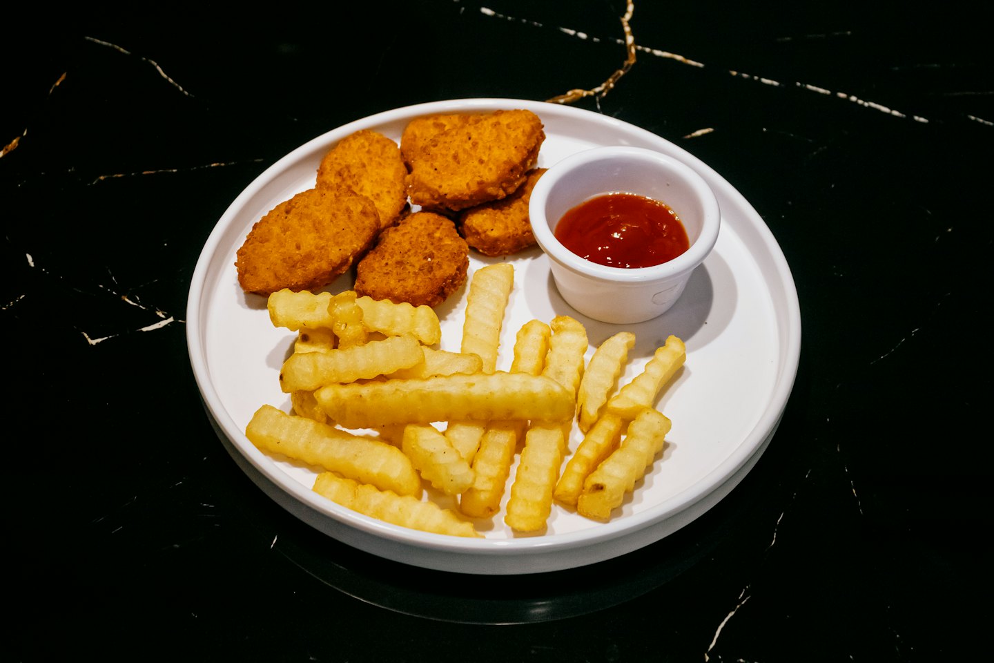 Golden chicken nuggets and fries on a white plate.