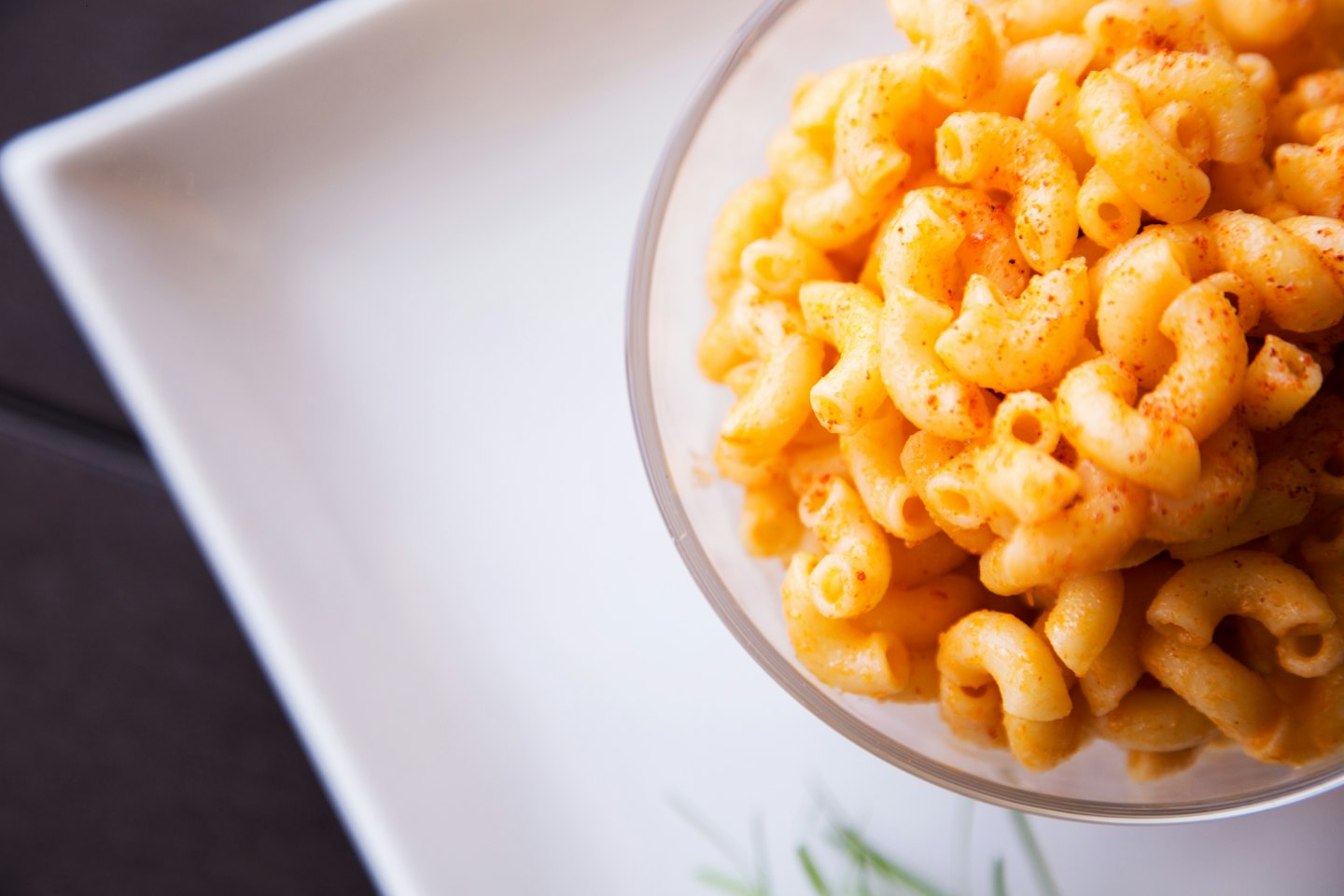 Creamy macaroni and cheese in a glass bowl with red seasoning.